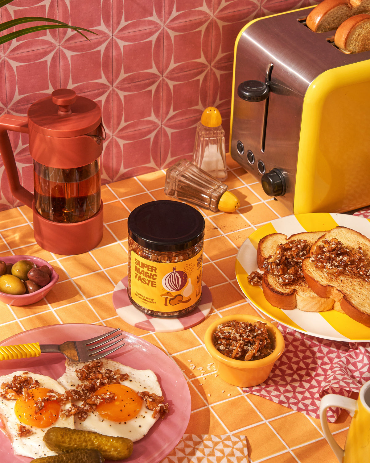 Fried eggs and buttered toast topped with Super Magic Taste Yummy Crisp, the no-heat mushroom crisp, with the jar in the middle of a yellow table.
