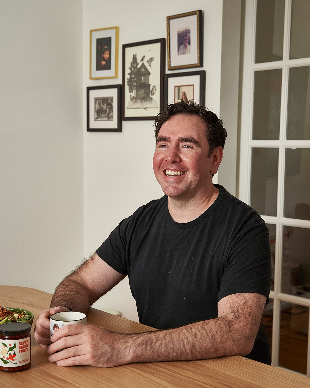 Co-founder Bruno Roldan del Bosque smiling at a table with a coffee mug and a jar of Super Magic Taste Chili Crisp