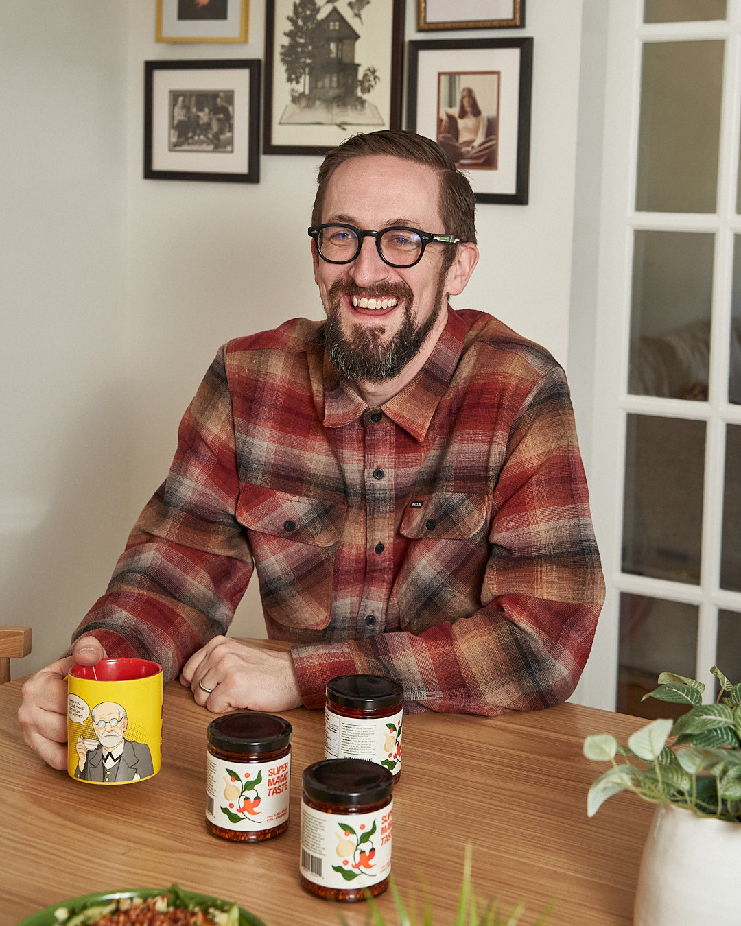 Co-founder Steven Michael Thomas laughing at a kitchen table with a mug and three jars of Super Magic Taste